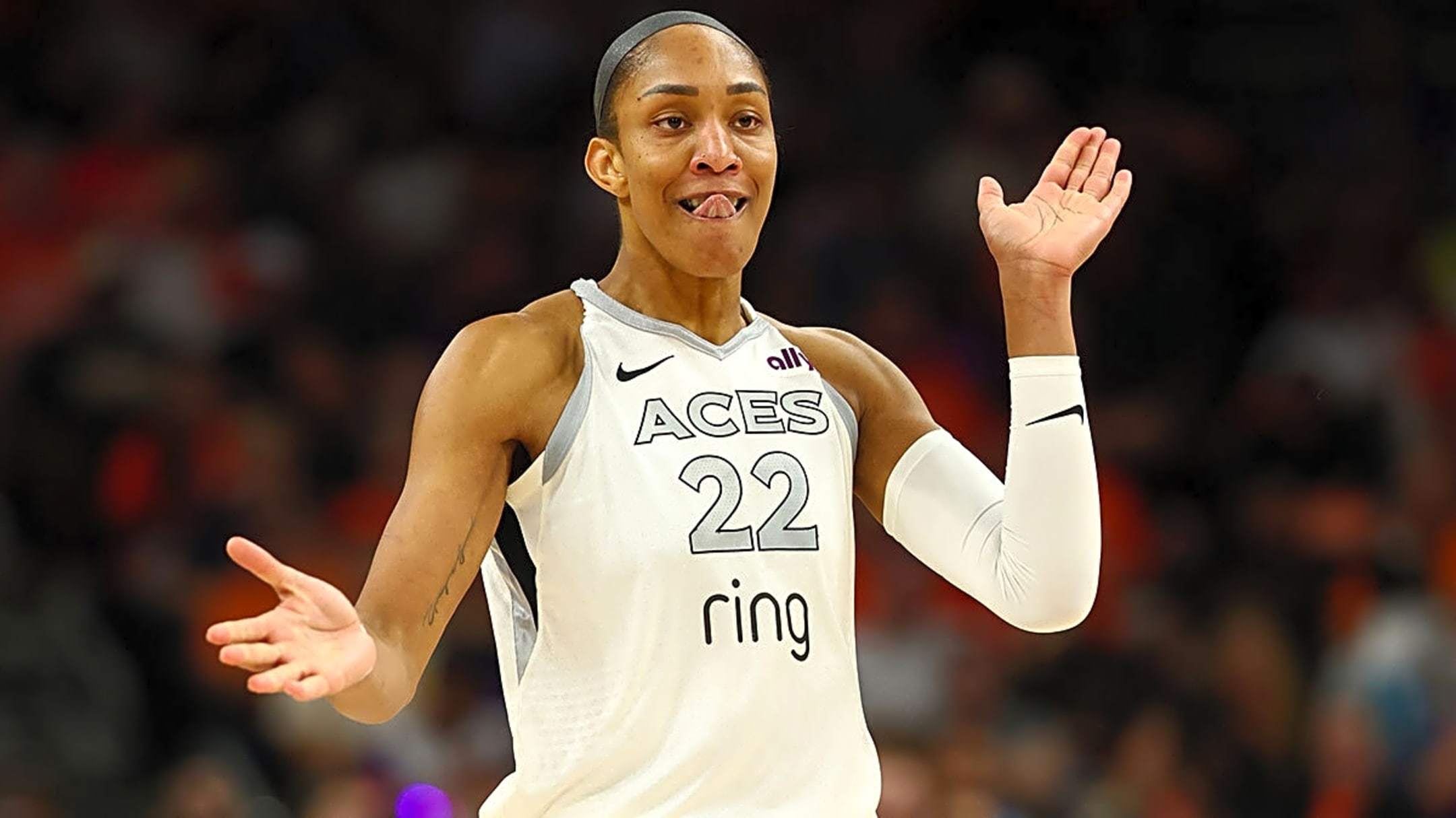 Basketball player wearing ACES jersey #22 with arms raised, on court and smiling playfully at the camera.