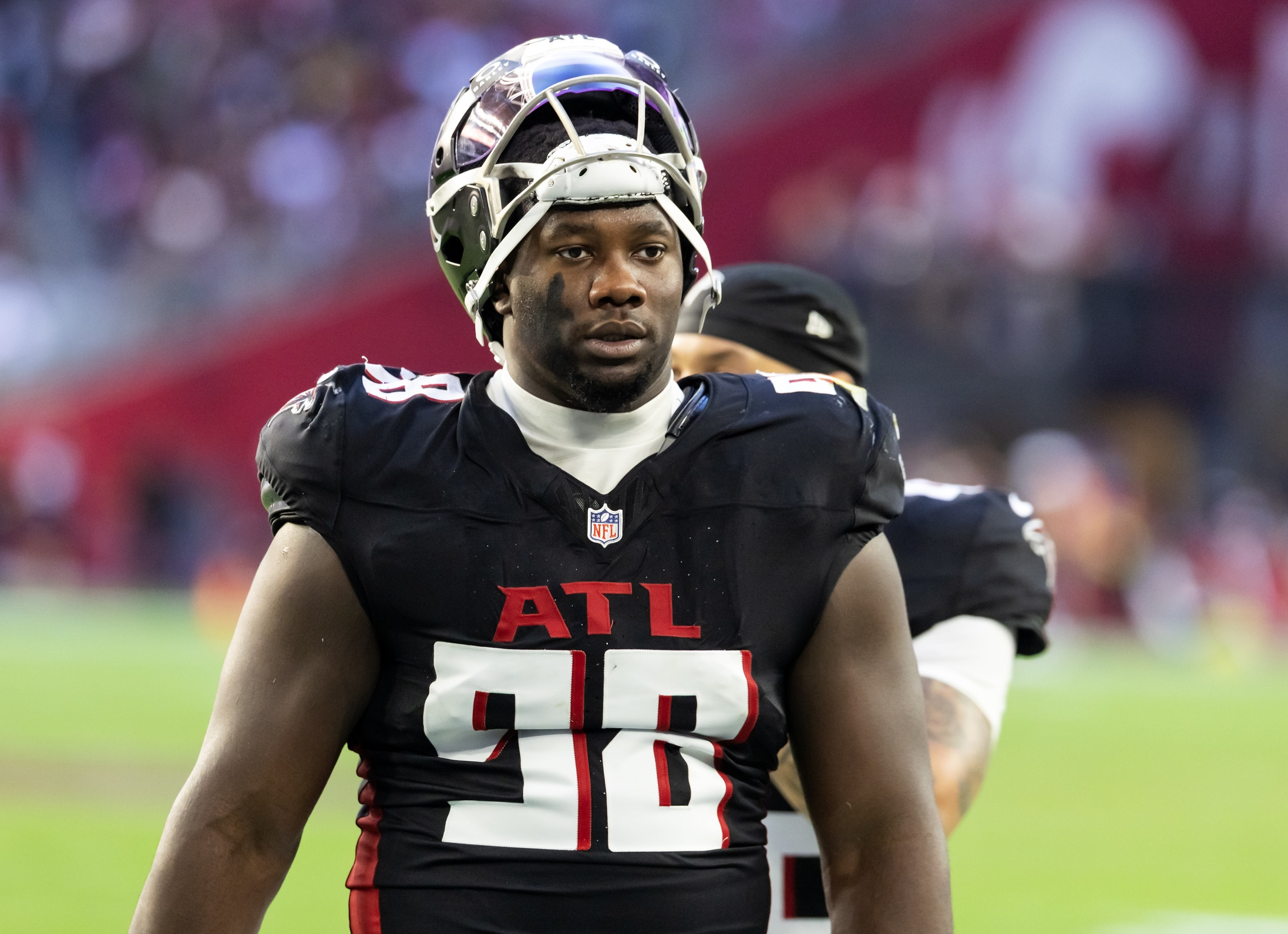 African American football player in Atlanta Falcons jersey #28 stands on the field wearing a helmet and black uniform with red and white detailing.