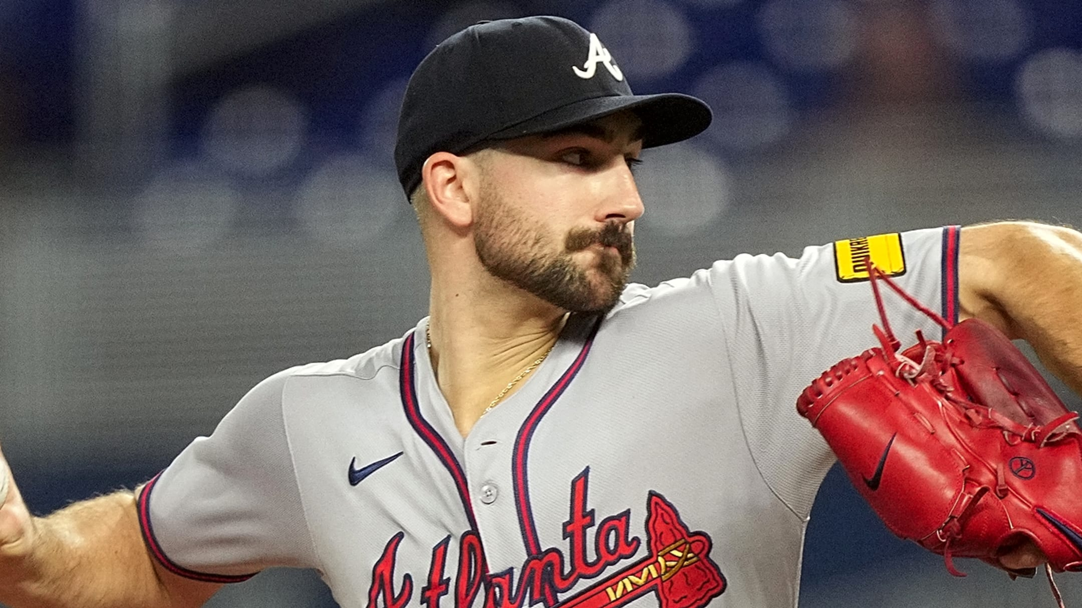 Baseball pitcher in a gray Atlanta Braves uniform throwing a pitch, with a red glove ready at his side.