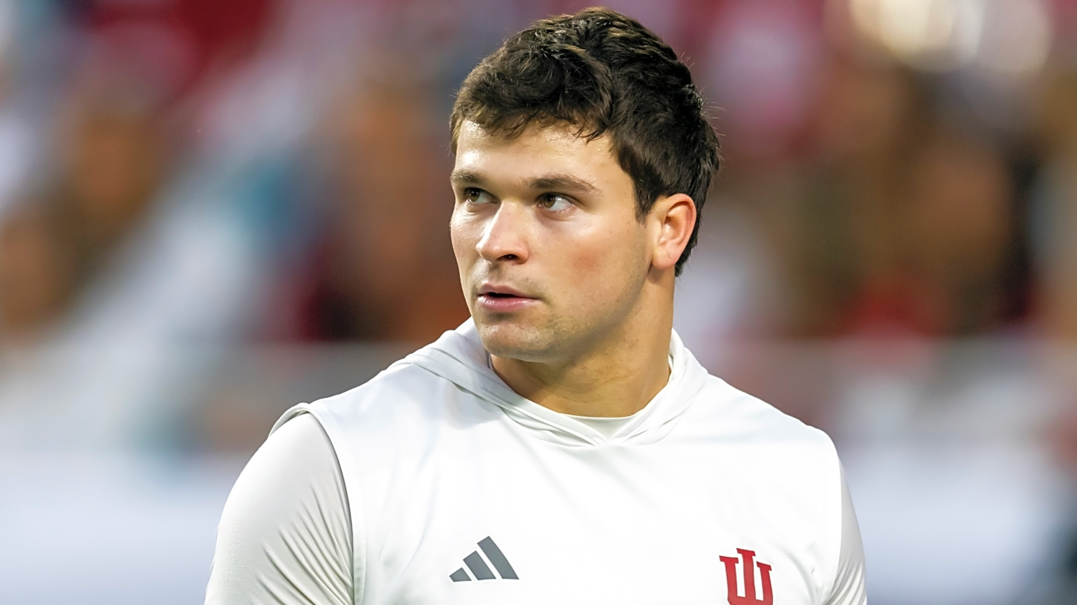 Male athlete in a white sleeveless top with IU logo, looking off to the left against a blurred stadium background.